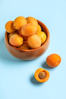 Bowl of ripe apricots on color background