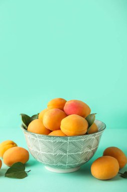 Bowl of tasty ripe apricots on color background