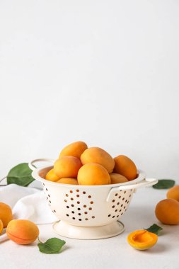 Colander with ripe apricots on light background