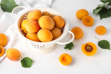 Colander with ripe apricots on light background