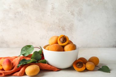 Bowl of tasty ripe apricots on light background
