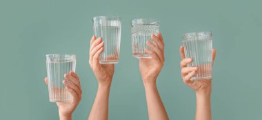 Female hands with glasses of water on green background