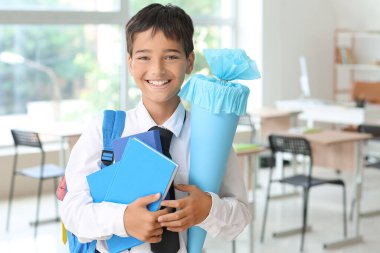 Little boy with blue school cone and books in classroom
