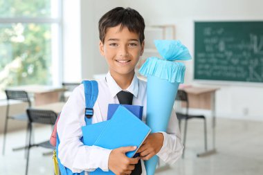 Little boy with blue school cone and books in classroom