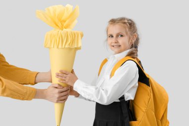 Mother greeting her little daughter with school cone on light background