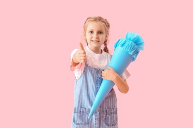 Cute little girl with blue school cone showing thumb-up on pink background