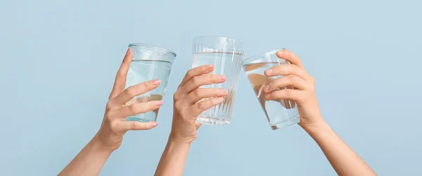 Female hands with glasses of water on light blue background
