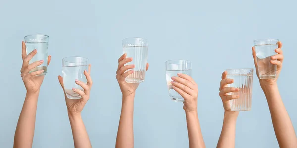 Female hands with glasses of water on light blue background