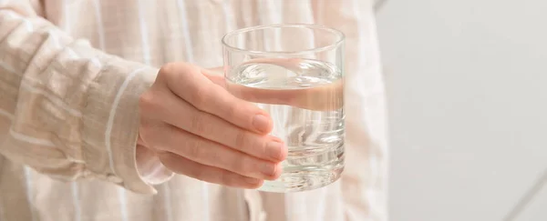 Woman with glass of fresh water on light background, closeup