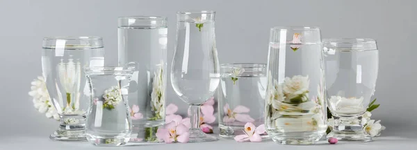 Glasses with water and flowers on light background