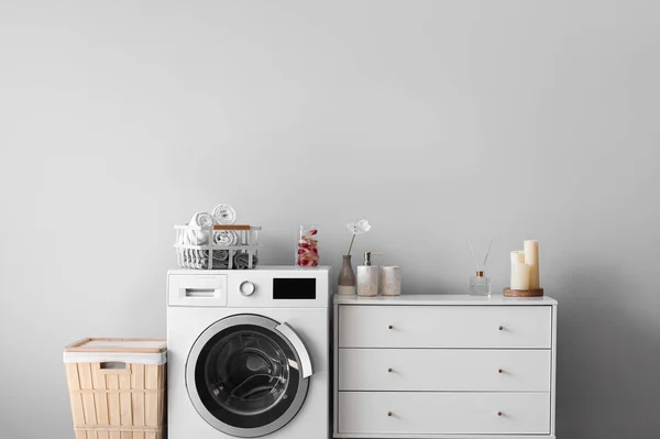 Interior of light laundry room with washing machine, basket and chest of drawers