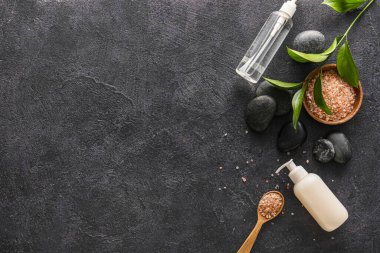 Composition with bottles of cosmetic products, spa stones and sea salt on dark background