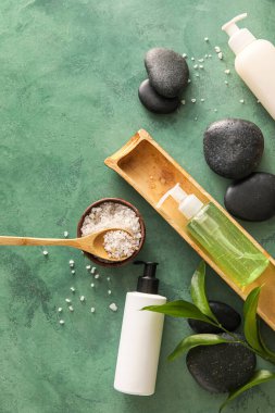 Composition with bottles of cosmetic products, sea salt and spa stones on color background