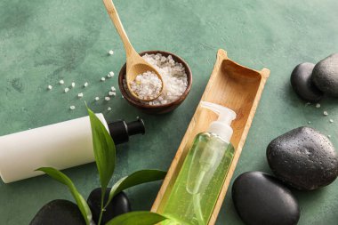 Composition with bottles of cosmetic products, sea salt and spa stones on color background