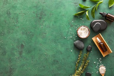 Composition with bottles of cosmetic products, sea salt and spa stones on green background