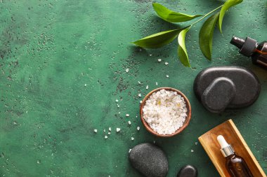 Composition with bottles of cosmetic products, sea salt and spa stones on green background