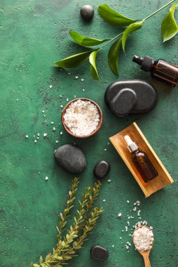 Composition with bottles of cosmetic products, sea salt and spa stones on green background