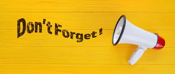 Megaphone and text DON'T FORGET on yellow wooden background