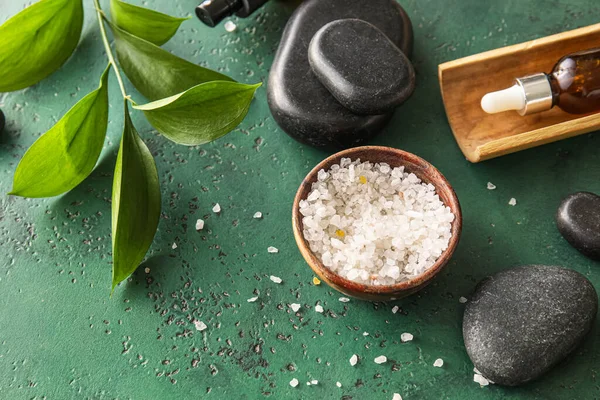 Bowl of sea salt and spa stones on green background