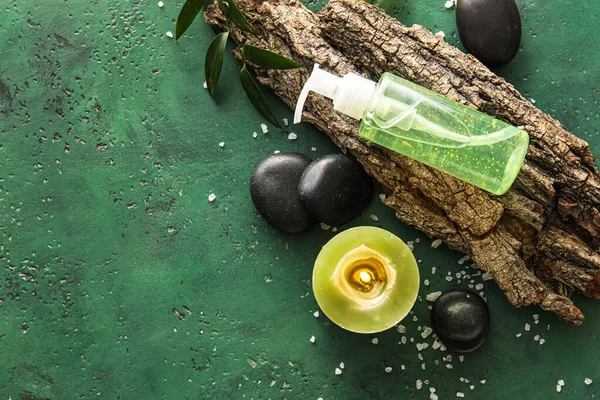 Composition with bottle of cosmetic product, burning candle, tree bark and spa stones on color background