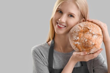 Young woman with fresh bread on grey background, closeup