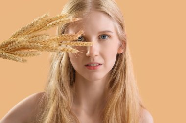 Young woman with wheat ears on beige background