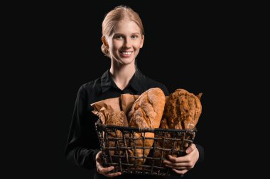Young woman holding basket with fresh bread on black background
