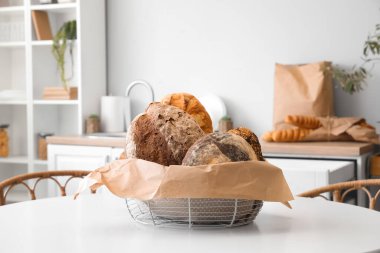 Basket with loaves of fresh bread and parchment paper on table in kitchen