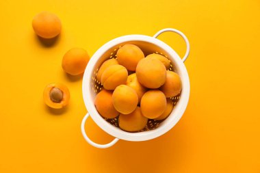 Colander of delicious apricots on color background