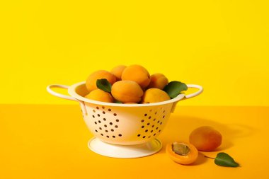 Colander with ripe apricots on color background