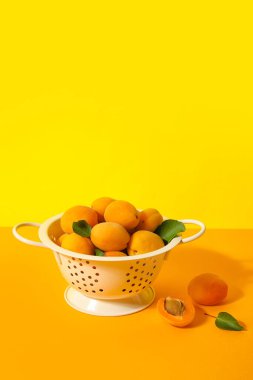 Colander with ripe apricots on color background