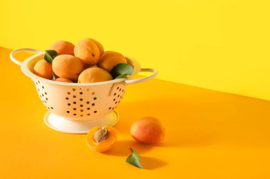 Colander with ripe apricots on color background