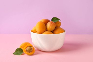 Bowl of delicious apricots on color background