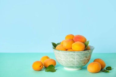 Bowl with ripe apricots on color background