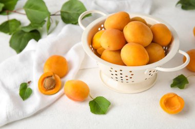 Colander with ripe apricots on light background