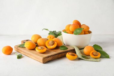 Wooden board and bowl of ripe apricots on light background