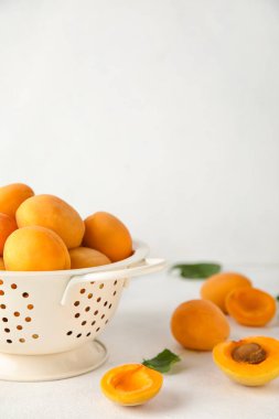 Colander with ripe apricots on light background, closeup