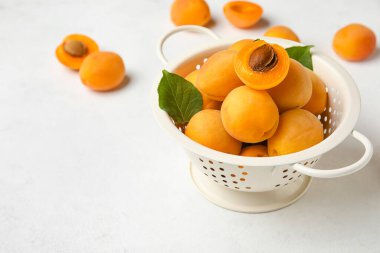 Colander full of ripe apricots on light background
