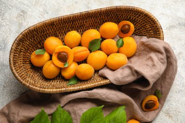 Wicker basket with ripe apricots on light background, closeup