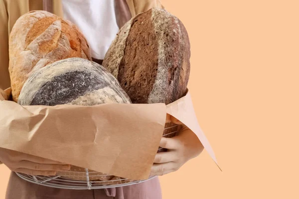 Young woman holding basket with fresh bread on beige background, closeup