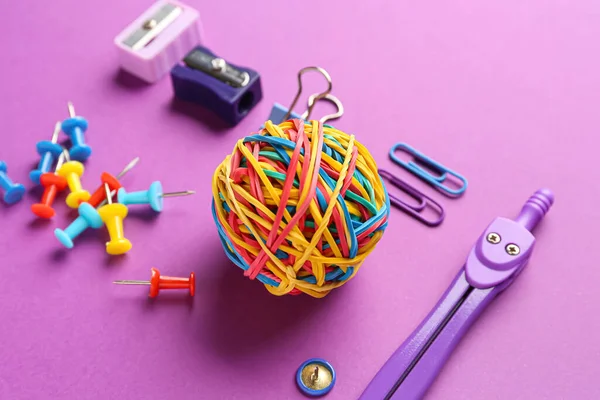 Colorful rubber band ball and stationery supplies on purple background