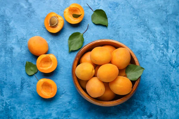 Bowl of delicious apricots on color background