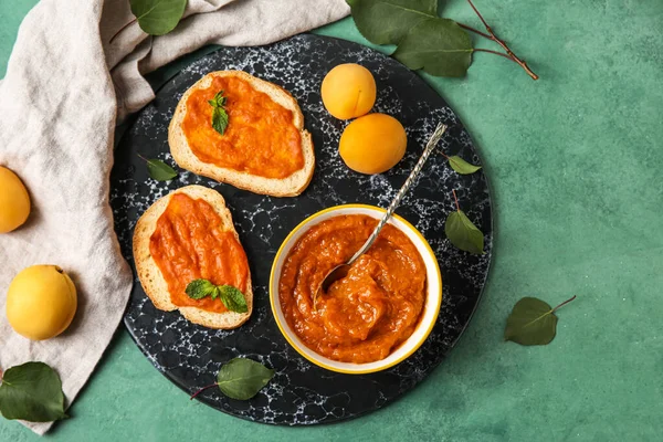 Composition with bowl of tasty apricot jam, sandwiches and fruits on color background