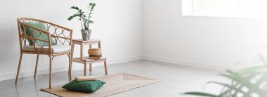Wicker chair with green pillows, books, stepladder and houseplant in light wall