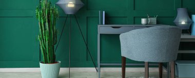 Comfortable workplace with armchair, lamps and cactus near green wall in room
