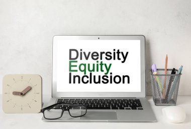 Modern laptop with text DIVERSITY, EQUITY, INCLUSION on screen at workplace