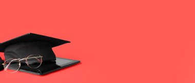 Graduation hat with tablet computer and eyeglasses on red background with space for text