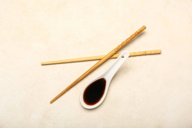 Spoon of soy sauce and chopsticks on light background