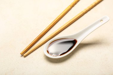 Spoon of soy sauce and chopsticks on light background