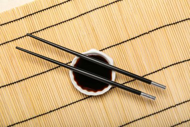 Bowl of soy sauce and chopsticks on bamboo mat